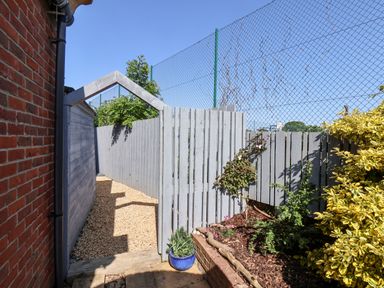 A gravel pathway beside a brick wall with a grey wooden fence and plants at Pond Farm View in Hinderwell