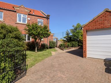 A brick house with a small tree and bushes beside a paved driveway and a detached garage at Pond Farm View in Hinderwell