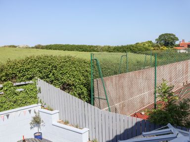 A backyard with a tennis court fenced off and a wooden fence beside a patio area with plants at Pond Farm View in Hinderwell