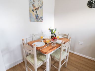 A dining area with a wooden table set with plates glasses of orange juice a bowl of strawberries and flowers on the table at Dryslwyn Cottage in Llandeilo
