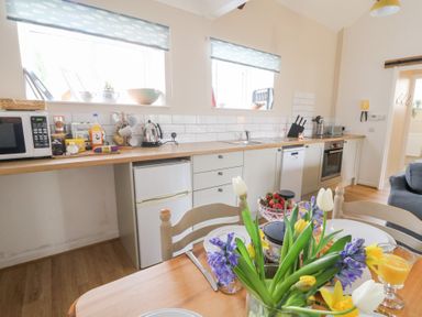 A kitchen with a countertop holding a microwave toaster kettle and knife set and a table with flowers and fruit at Dryslwyn Cottage in Llandeilo