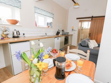 A kitchen and dining area with a wooden table set with plates glasses flowers and coffee at Dryslwyn Cottage in Llandeilo