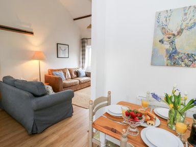 A dining table set with plates and glasses beside a living room with two sofas and a floor lamp at Dryslwyn Cottage in Llandeilo