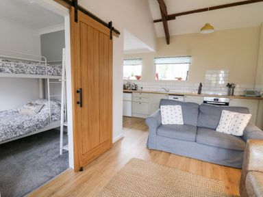 A kitchen and living room with a sofa and bunk beds behind a sliding wooden door at Dryslwyn Cottage in Llandeilo