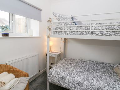 A bedroom with bunk beds a bedside table with a lamp and a wicker chair with towels at Dryslwyn Cottage in Llandeilo