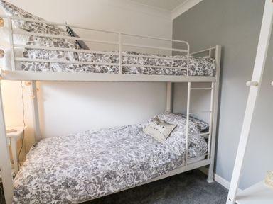 A bedroom with a white metal bunk bed with floral bedding and a small side table at Dryslwyn Cottage in Llandeilo