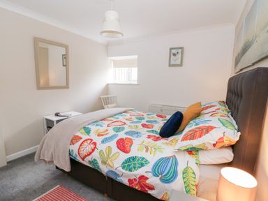 A bedroom with a bed with colorful leaf patterned bedding a chair a side table and a window at Dryslwyn Cottage in Llandeilo