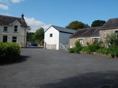 A gravel courtyard with cream building small white building and stone building with plants at Dinefwr Cottage Golden Grove near Llandeilo