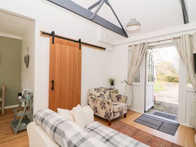 A living area with a sofa, armchair, sliding wooden door, and open double doors leading outside at Dinefwr Cottage Golden Grove near Llandeilo