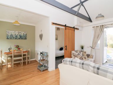 A dining area with a wooden table set for two next to a living room with a sliding wooden door and chairs at Dinefwr Cottage in Golden Grove near Llandeilo