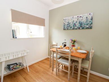 A dining area with a wooden table and four chairs set with plates glasses and flowers at Dinefwr Cottage in Golden Grove near Llandeilo