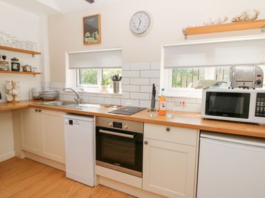 A kitchen with white cabinets wooden countertops a sink two windows a microwave an oven a toaster and dishes at Dinefwr Cottage Golden Grove near Llandeilo