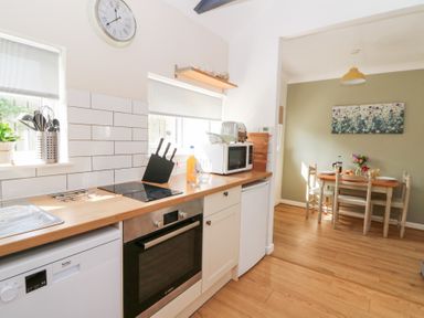 A kitchen area with stove oven microwave and utensils next to a dining table with chairs and flowers at Dinefwr Cottage Golden Grove near Llandeilo