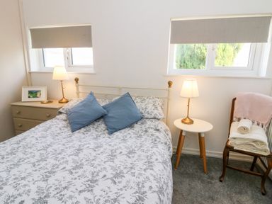 A bedroom with a bed blue pillows two bedside tables lamps a chest of drawers and a chair with folded towels at Dinefwr Cottage Golden Grove near Llandeilo