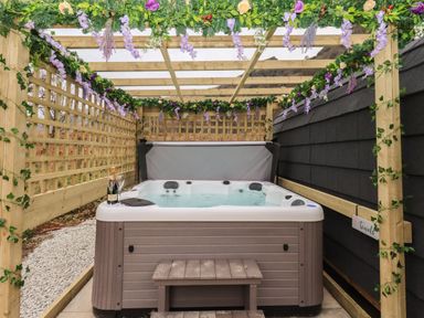 An outdoor hot tub under a wooden pergola decorated with flowers and greenery at The Stag - Crossgate Luxury Glamping Hartsop near Glenridding