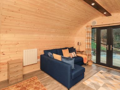 A living area with a blue sofa with pillows near glass doors and wooden walls at The Stag - Crossgate Luxury Glamping Hartsop near Glenridding