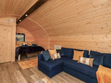A wooden room with a blue sofa and bed with pillows at The Stag - Crossgate Luxury Glamping in Hartsop near Glenridding
