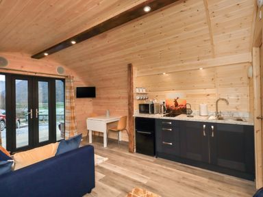 An open wooden interior with a kitchenette a small dining table a blue sofa and glass doors at The Stag - Crossgate Luxury Glamping in Hartsop near Glenridding