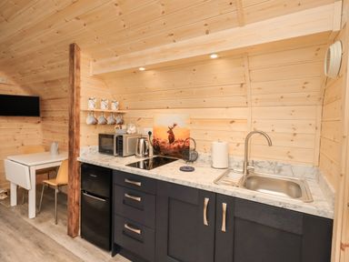 A kitchen area with black cabinets a stainless steel sink microwave kettle and a small dining table with chairs at The Stag - Crossgate Luxury Glamping Hartsop near Glenridding