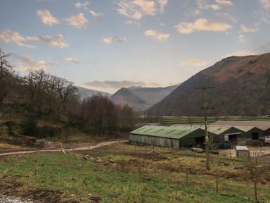 A rural farm scene with green metal barns surrounded by fields and hills at The Stag - Crossgate Luxury Glamping in Hartsop near Glenridding
