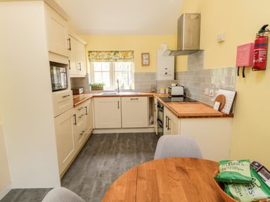 A kitchen with cream cabinets wooden countertops a round wooden table and yellow walls at Kizzie Cottage in Guyzance near Warkworth