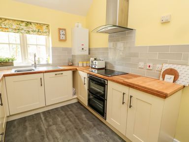 A kitchen with cream cabinets wooden countertops a stove toaster and a window with floral blinds at Kizzie Cottage in Guyzance near Warkworth