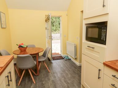 A kitchen with wooden table and gray chairs next to an open door and microwave at Kizzie Cottage Guyzance near Warkworth
