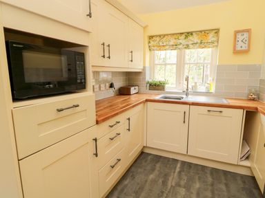 A kitchen with wooden countertops white cabinets a microwave a sink under a window and a clock on the wall at Kizzie Cottage in Guyzance near Warkworth