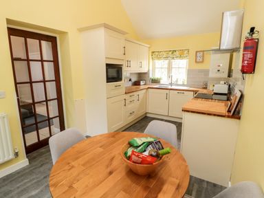 A kitchen with wooden round table and chairs cooking area with cabinets and window at Kizzie Cottage in Guyzance near Warkworth