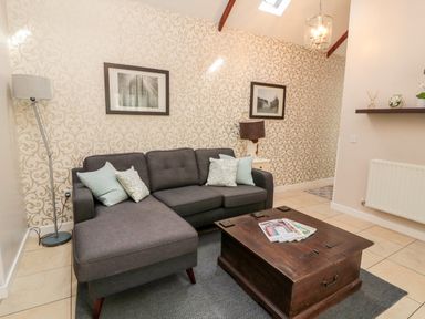 A living room with a gray sectional sofa and pillows a wooden coffee table and patterned wallpaper at Kizzie Cottage in Guyzance near Warkworth