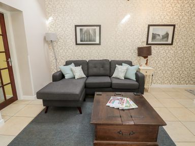 A living room with a gray sectional sofa and a wooden coffee table with magazines at Kizzie Cottage Guyzance near Warkworth