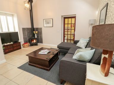 A living room with a dark sofa and cushions a wooden coffee table a wood burning stove and a television at Kizzie Cottage in Guyzance near Warkworth