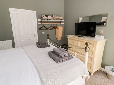 A bedroom with a bed, folded towels, a dresser with a television, a mirror, and a wall-mounted rack with hangers and folded blankets at Kizzie Cottage in Guyzance near Warkworth