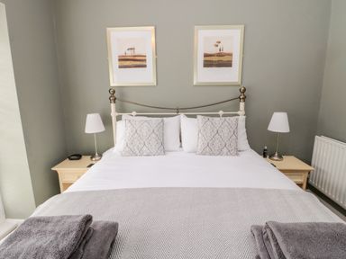 A bedroom with a bed with pillows and a blanket two bedside tables with lamps and framed pictures on the wall at Kizzie Cottage in Guyzance near Warkworth