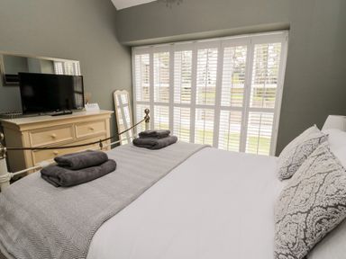 A bedroom with a bed with folded towels a dresser with a tv and a standing mirror near windows with shutters at Kizzie Cottage Guyzance near Warkworth