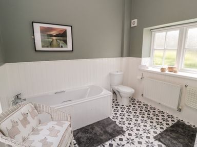 A bathroom with a bathtub toilet wicker chair and window at Kizzie Cottage in Guyzance near Warkworth
