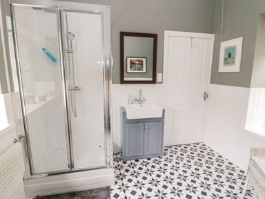 A bathroom with a glass shower enclosure a sink with cabinet and a door on a patterned tile floor at Kizzie Cottage Guyzance near Warkworth