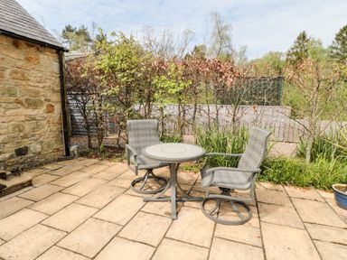 A patio with two chairs and a round table next to a stone wall at Kizzie Cottage in Guyzance near Warkworth