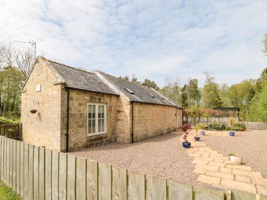 A stone cottage with a gravel yard and potted plants along a paved path at Kizzie Cottage in Guyzance near Warkworth