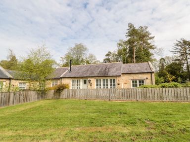 A stone cottage with white windows and a wooden fence in front with a grassy yard at Kizzie Cottage Guyzance near Warkworth