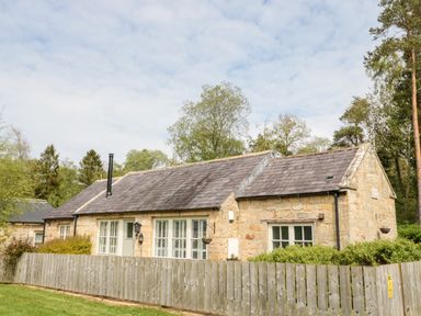 A stone cottage with a slate roof surrounded by a wooden fence and greenery at Kizzie Cottage in Guyzance near Warkworth