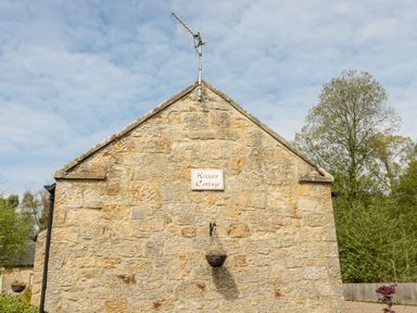 The stone wall of Kizzies Cottage with a sign and television antenna Guyzance near Warkworth