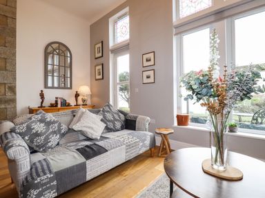 A living room with a patterned sofa, wooden coffee table with flowers, a sideboard with decorative items and a wall mirror at King Edward's View in Newquay