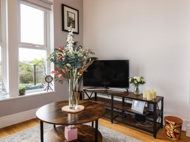 A corner of a living room with a TV on a wooden stand and flowers in glass vases at King Edward's View in Newquay