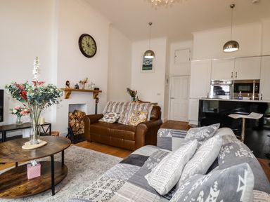 A living room with two sofas a coffee table with flowers and a kitchen in the background at King Edward's View in Newquay