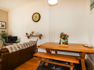 A living room with a brown leather sofa wooden dining table and bench a wall clock and decorative items at King Edward's View in Newquay