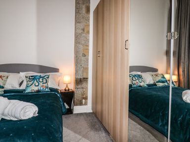 A bedroom with a bed with ocean themed pillows a nightstand with a lamp and a wardrobe with mirrored doors at King Edward's View in Newquay