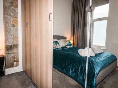 A bedroom with a bed with teal bedding and rolled towels next to a wooden wardrobe and window at King Edward's View in Newquay
