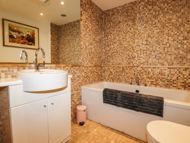 A bathroom with a white sink, bathtub, and mosaic tiled walls at King Edward's View in Newquay