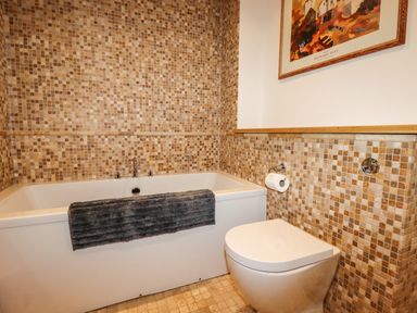 A bathroom with a bathtub a toilet and mosaic tiled walls at King Edward's View in Newquay